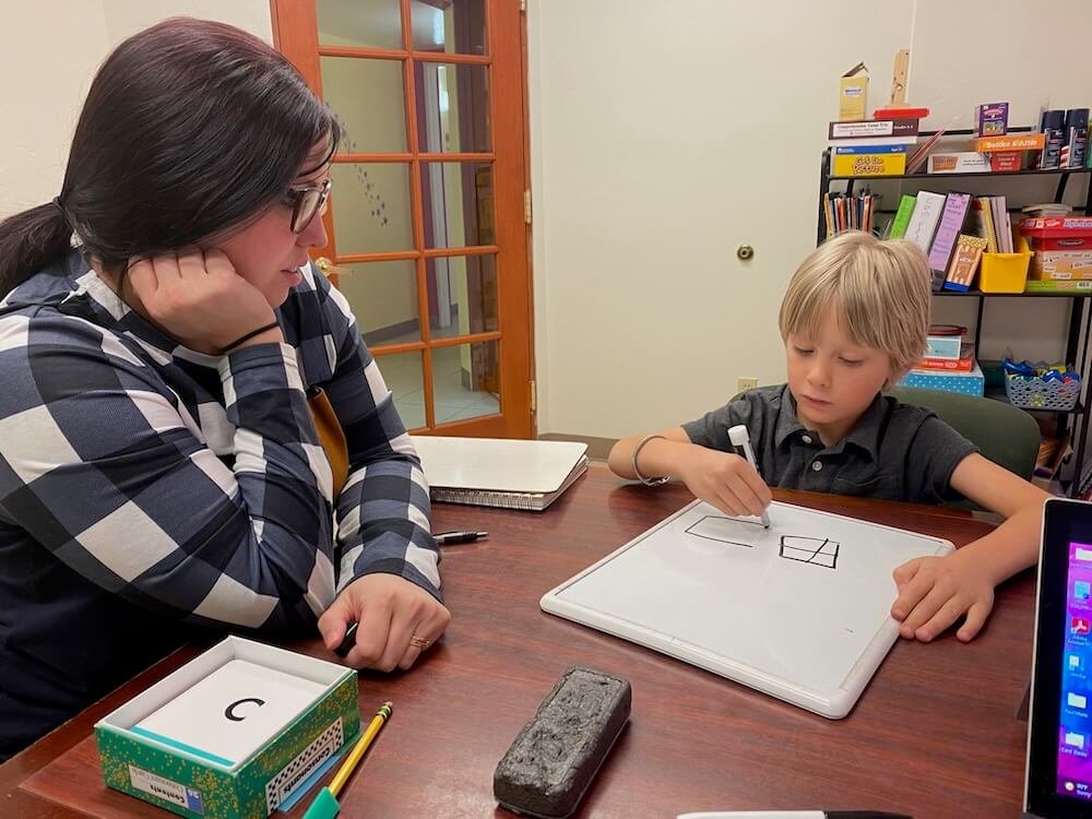 Preschooler with tutor drawing shapes